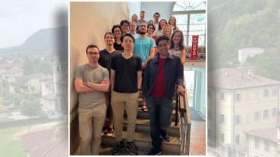 A group of diverse students and faculty pose together on a staircase inside a bright building at the Steger Center for International Scholarship, Virginia Tech. A banner reading 'VT Invent the Future Hokies' is visible beside them, and a window behind them lets in natural light. Everyone is smiling. The Virginia Tech logo and Steger Center branding appear at the top of the image.