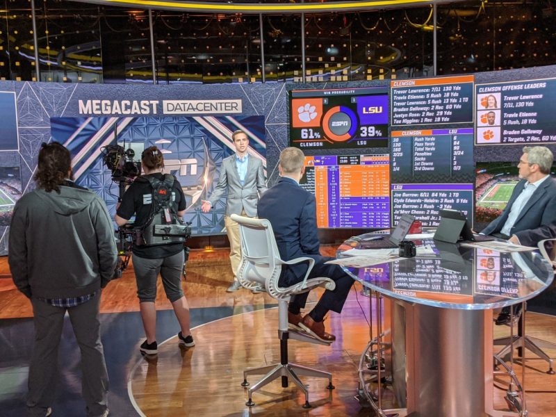 Dressed in a suit, Paul Sabin stands on the air at the ESPN studio. Camera crews and production managers surround him, off camera.Photo courtesy Sabin. 