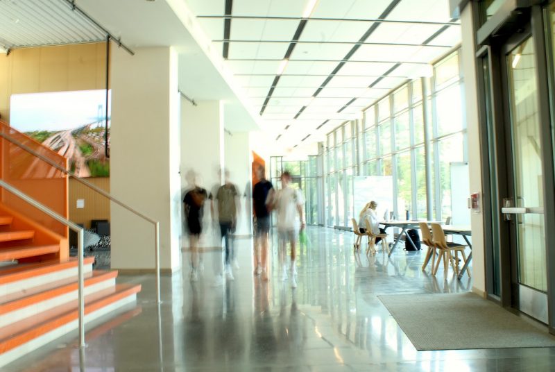 Four students (blurred) walk down a hallway as a female student sits nearby at a table working inside the Creativity and Innovation District.